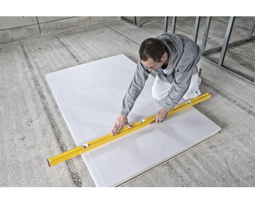 Artisan découpant une plaque de plâtre avec un cutter et un niveau à bulle sur un chantier de construction.