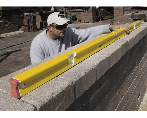 Artisan utilisant un long niveau à bulle pour contrôler l'horizontalité d'un mur en pierre.