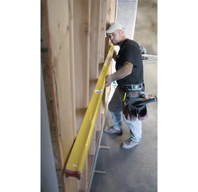 Un ouvrier du bâtiment utilise un long niveau à bulle jaune pour vérifier l'alignement d'une cloison en bois sur un chantier.