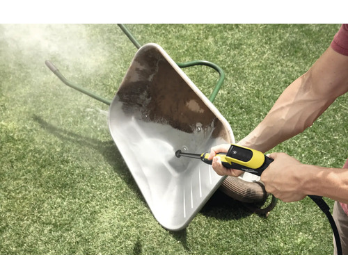 Reinigung einer verschmutzten Schubkarre auf einer Rasenfläche mit einem Hochdruckreiniger.