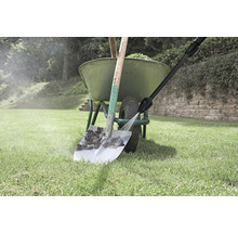 Ein Hochdruckreiniger reinigt eine verschmutzte Schaufel vor einer grünen Schubkarre auf einer Rasenfläche.