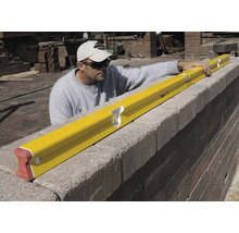 Artisan utilisant un long niveau à bulle pour contrôler l'horizontalité d'un mur en pierre.