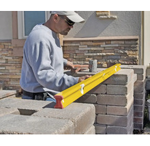 Une personne utilise un niveau à bulle jaune pour vérifier l'alignement de blocs de pierre lors de la construction d'un mur.