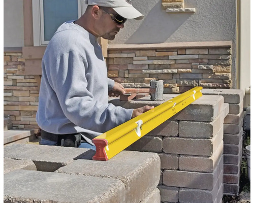 Une personne utilise un niveau à bulle jaune pour vérifier l'alignement de blocs de pierre lors de la construction d'un mur.