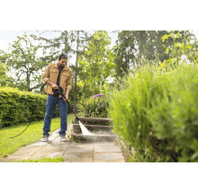 Un homme nettoie des marches en pierre dans un jardin avec un nettoyeur haute pression dans un cadre lumineux.