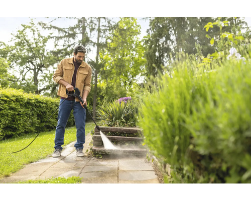 Un homme nettoie des marches en pierre dans un jardin avec un nettoyeur haute pression dans un cadre lumineux.