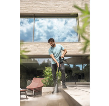 Un homme nettoie une terrasse en pierre claire devant une maison moderne avec un nettoyeur haute pression.
