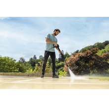 Un homme nettoie une terrasse en pierre claire dans le jardin avec un nettoyeur haute pression par temps ensoleillé.