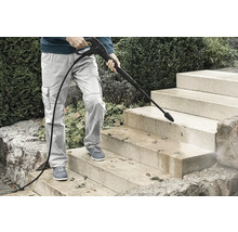 Personne nettoyant un escalier extérieur en pierre avec un nettoyeur haute pression pour enlever la saleté et les feuilles.