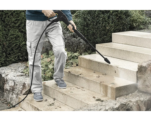Personne nettoyant un escalier extérieur en pierre avec un nettoyeur haute pression pour enlever la saleté et les feuilles.