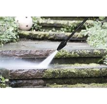 Nettoyeur haute pression qui nettoie des marches en pierre recouvertes de mousse avec un jet eau puissant.