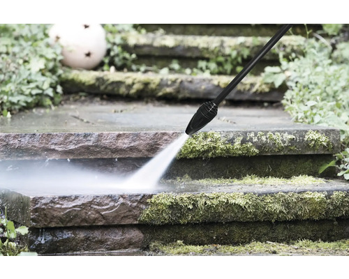 Nettoyeur haute pression qui nettoie des marches en pierre recouvertes de mousse avec un jet eau puissant.