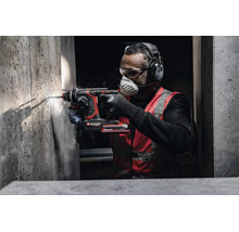 Un artisan utilise un perforateur sans fil Einhell pour percer un mur en béton avec un équipement de protection comme un casque antibruit.