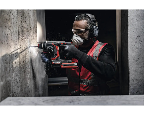 Un artisan utilise un perforateur sans fil Einhell pour percer un mur en béton avec un équipement de protection comme un casque antibruit.