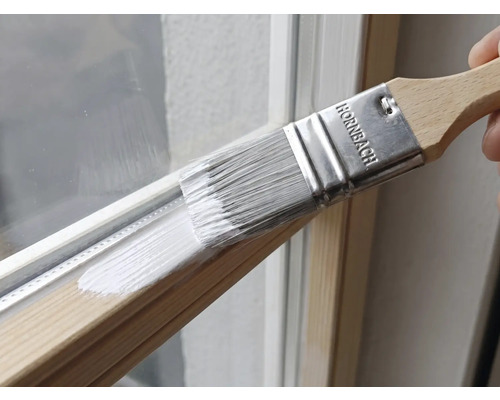Pinceau plat Hornbach appliquant de la peinture blanche sur un cadre de fenêtre en bois.