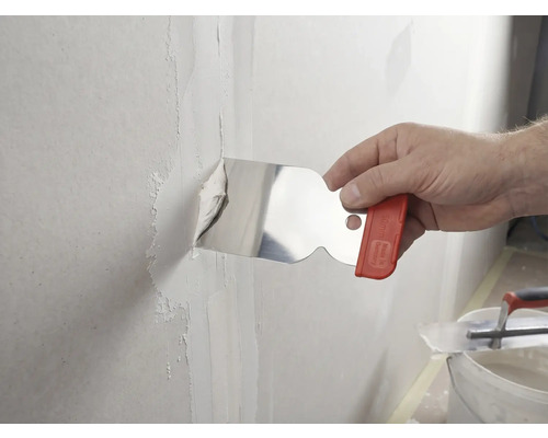 Une main applique de l'enduit sur un joint de mur à l'aide d'un couteau à enduire en acier inoxydable.