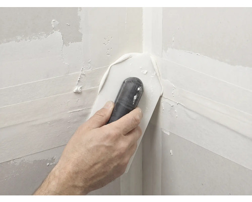 Main utilisant une truelle d angle pour lisser l enduit dans un angle intérieur de plaques de plâtre.