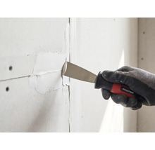Une main gantée utilise un couteau de peintre Rautner pour jointer des plaques de plâtre.