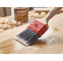 Pinceau RAUTNER appliquant du vernis sur une surface en bois. Avec des poils synthétiques, un manche en bois et une virole rouge.