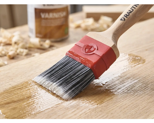 Pinceau RAUTNER appliquant du vernis sur une surface en bois. Avec des poils synthétiques, un manche en bois et une virole rouge.