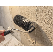 Rouleau à crépir lors de l'application d'un enduit de parement sur un mur rugueux.