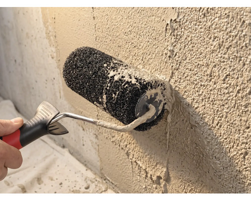 Rouleau à crépir lors de l'application d'un enduit de parement sur un mur rugueux.