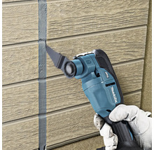 Makita Multifunktionsgeschier beim Ewechhuele vun Dichtstoff tëscht Wandpaneelen mat Holzstruktur.