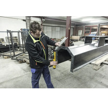 Artisan dans un atelier utilisant un rapporteur d angle numérique pour mesurer avec précision une grande structure métallique sur une palette.
