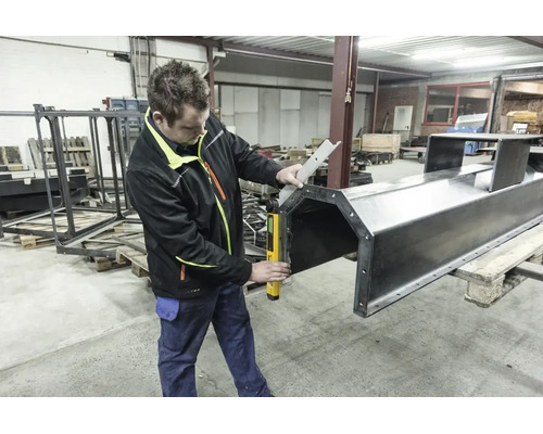 Artisan dans un atelier utilisant un rapporteur d angle numérique pour mesurer avec précision une grande structure métallique sur une palette.