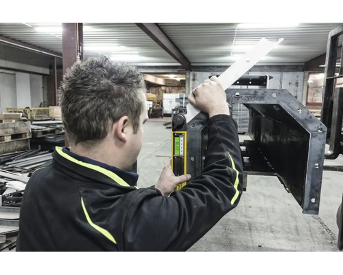 Une personne utilise un rapporteur d'angle numérique pour mesurer une pièce métallique dans un atelier lumineux.