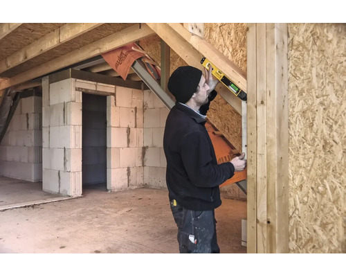 Artisan utilisant un niveau à bulle numérique avec STABILA Logo sur une poutre en bois dans un bâtiment brut avec parois en béton cellulaire.