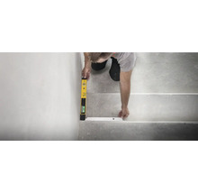 Une personne utilise un niveau à bulle numérique pour aligner un profilé de nez de marche sur un escalier en béton.