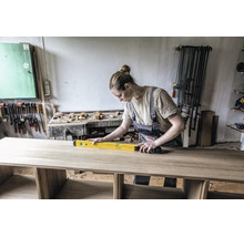 Artisane vérifiant l'alignement d'un plateau en bois à l'aide d'un niveau à bulle dans un atelier bien organisé.