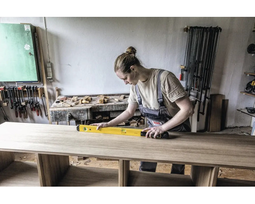 Artisane vérifiant l'alignement d'un plateau en bois à l'aide d'un niveau à bulle dans un atelier bien organisé.
