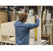Personne vérifiant l'alignement vertical d'un meuble en bois avec un niveau à bulle numérique dans un atelier.