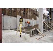 Laser rotatif Stabila sur trépied sur un chantier avec un ouvrier effectuant des mesures sur un mur en béton.