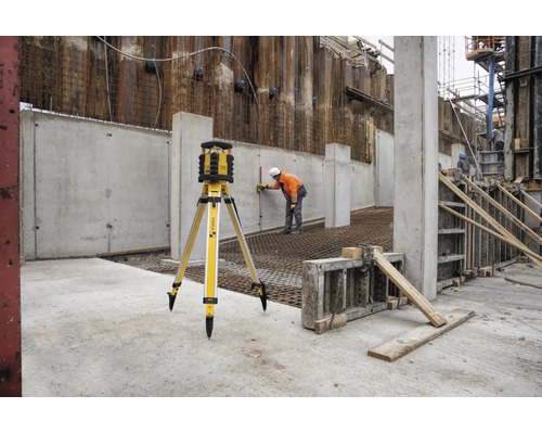 Laser rotatif Stabila sur trépied sur un chantier avec un ouvrier effectuant des mesures sur un mur en béton.