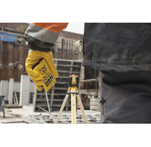 Main tenant une télécommande Stabila pour laser rotatif sur un chantier, avec un laser sur trépied en arrière-plan.