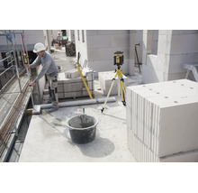 Ouvrier utilisant un laser rotatif sur trépied pour des mesures sur un chantier avec des blocs de béton cellulaire.
