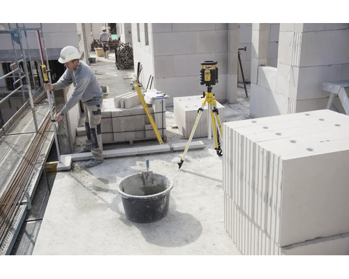 Ouvrier utilisant un laser rotatif sur trépied pour des mesures sur un chantier avec des blocs de béton cellulaire.