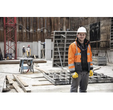 Ouvrier du bâtiment sur un chantier portant un casque de protection blanc, une veste haute visibilité et des gants de travail.