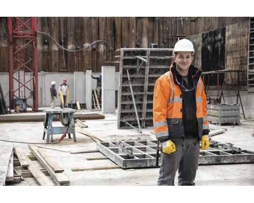 Ouvrier du bâtiment sur un chantier portant un casque de protection blanc, une veste haute visibilité et des gants de travail.