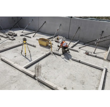 Ouvrier sur un chantier utilisant un laser rotatif et une mire pour aligner des blocs sur une dalle en béton.