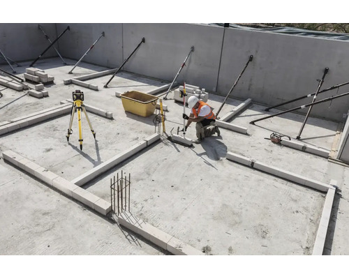 Ouvrier sur un chantier utilisant un laser rotatif et une mire pour aligner des blocs sur une dalle en béton.