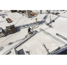 Ouvrier sur un chantier de construction en béton utilisant un laser rotatif et une mire pour le nivellement.
