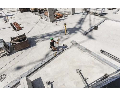 Ouvrier sur un chantier de construction en béton utilisant un laser rotatif et une mire pour le nivellement.