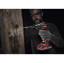 Perceuse-visseuse sans fil Einhell utilisée sur une poutre en bois par une personne portant un gant de travail et des lunettes de sécurité.