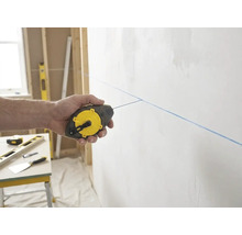 Main utilisant un cordeau à tracer Stanley pour marquer une ligne bleue sur un mur dans un environnement de chantier clair et organisé.
