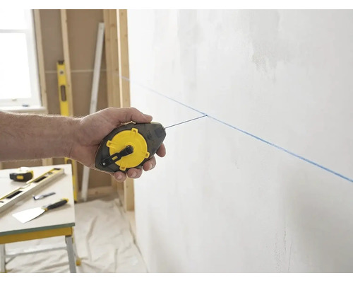 Main utilisant un cordeau à tracer Stanley pour marquer une ligne bleue sur un mur dans un environnement de chantier clair et organisé.
