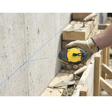 Artisan marquant une ligne droite avec un cordeau à tracer sur un mur en béton sur un chantier avec de la maçonnerie.